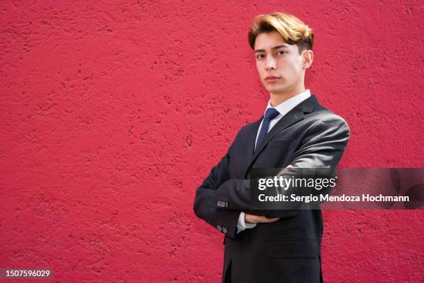young latino man in a suit and tie looking at the camera with arms crossed, serious, defiant, powerful - industrie de la mode photos et images de collection