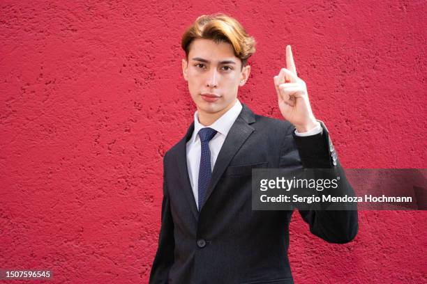 young latino man in a suit and tie looking at the camera and giving the number one sign, i voted - guy with attitude mid shot stock-fotos und bilder