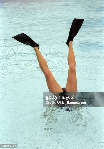 Symbolic photo to the topic " Freizeit / Urlaub ": A woman wearing fins is making a handstand in the water of a swimming pool.