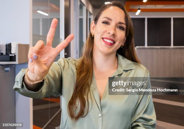 latino woman smiling, looking at the camera and giving the peace sign - cnd sign stock pictures, royalty-free photos & images