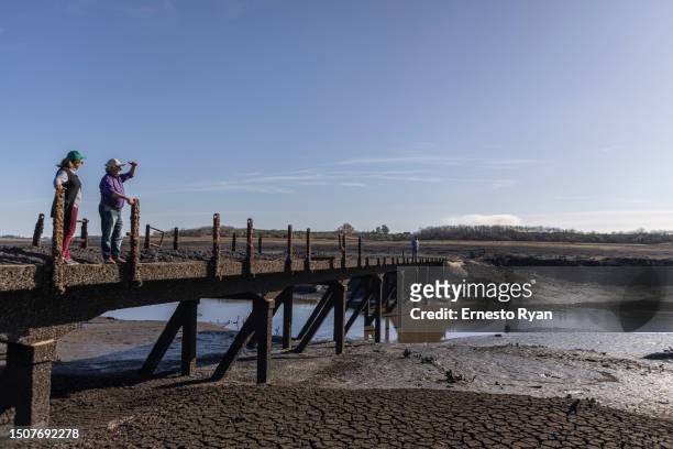 People stand on a bridge that emerged after 30 years of being under water of Santa Lucia river at Paso Severino reservoir on July 01, 2023 in...