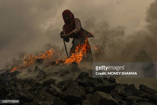 Girl burns raw coal to make it usable for further sale near an open cast mining site on the outskirts of Dhanbad on July 6, 2023.