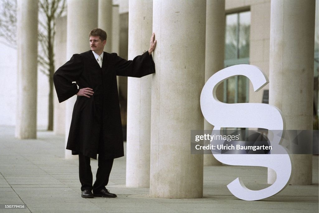 Symbolic photo to the topics: justice, law, etc,, Man in black robe with section mark standing between columns.