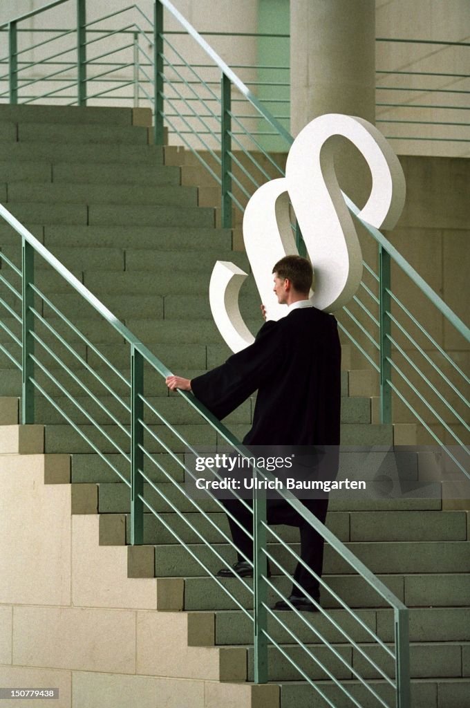 Symbolic photo to the topics: justice, law, etc,, Man in black robe with section mark on his shoulder walking up stairs.