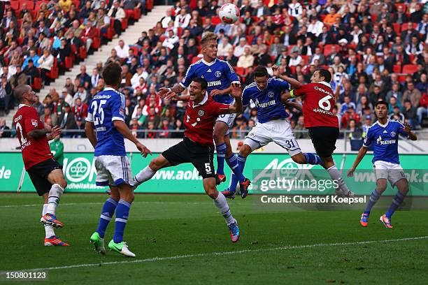 Lewis Holtby of Schalke scores the second goal against Mario Eggimann of Hannover and Steven Cherundolo of Hannover during the Bundesliga match...