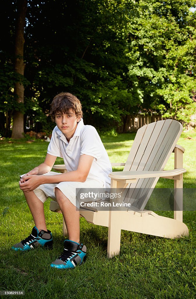 Teen boy sitting on adirondack chair in backyard