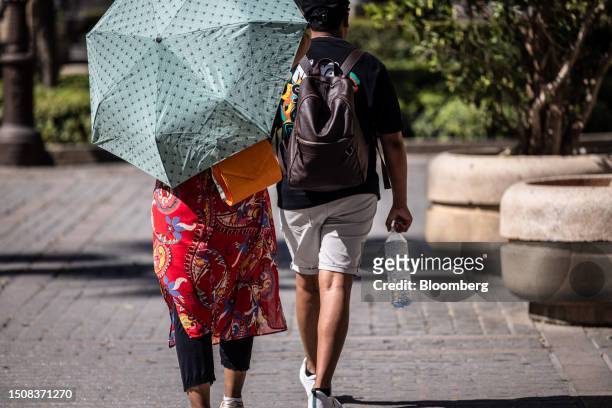 Visitors carry a water bottle and a umbrella during high temperatures near the cathedral in Seville, Spain, on Wednesday, July 5, 2023. Global...