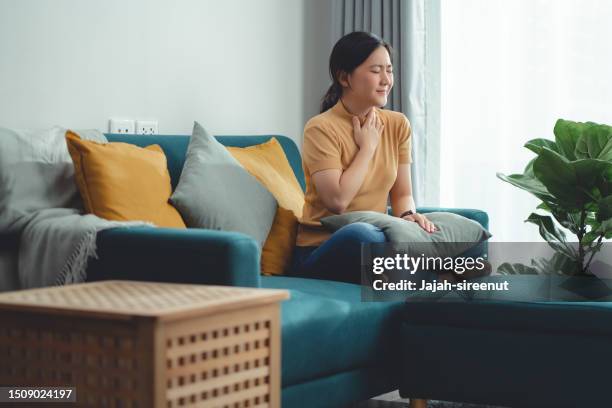 asian woman was sick with fever having sore throat sitting on sofa in living room at home. - slijm stockfoto's en -beelden