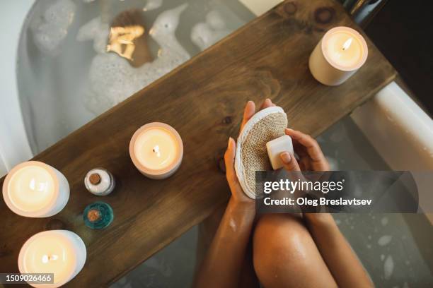 bath sponge and soap in female hands. bath tub, decorated with burning candles - loofah fotografías e imágenes de stock