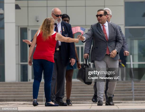 Rep. George Santos is presented with a miniature American flag as he departs federal court with his attorney Joseph Murray, rear right, on June 30 in...