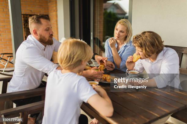 young family with two children having breakfast at back yard of house. summer picnic. - new cherry stockfoto's en -beelden