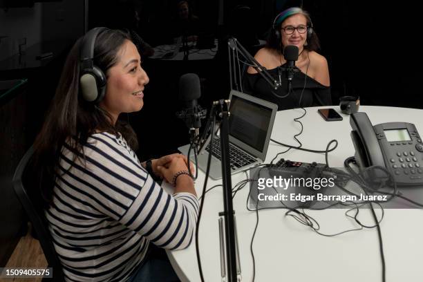 two adult women recording a podcast sitting at a table, using microphones and an audio recorder - live broadcast stock-fotos und bilder