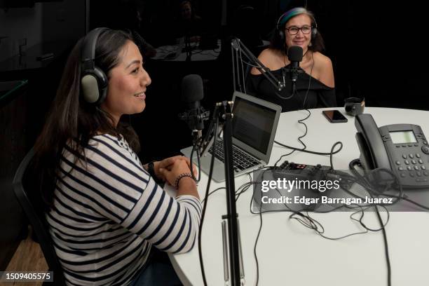 two adult women recording a podcast sitting at a table, using microphones and an audio recorder - live broadcast stock pictures, royalty-free photos & images