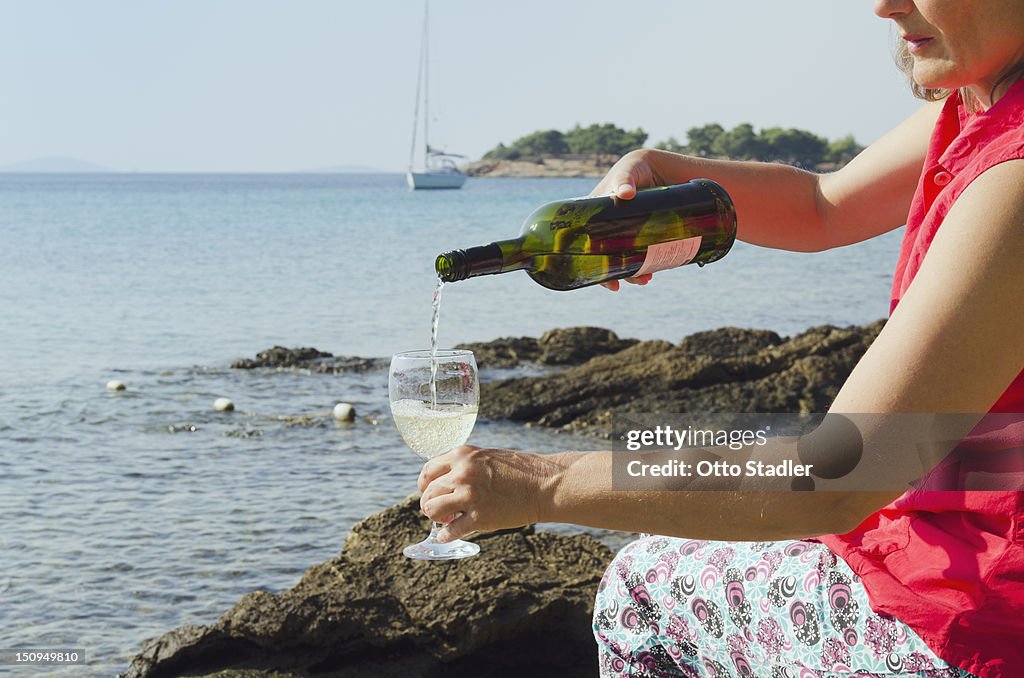 A woman pouring wine into a glass by the sea