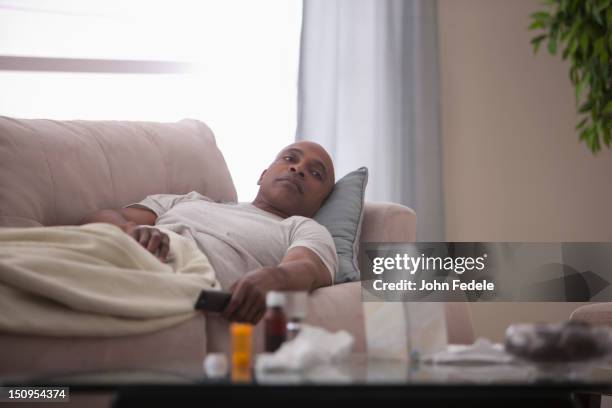 sick black man laying on sofa - rest cure foto e immagini stock