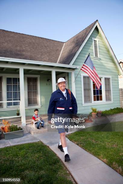 caucasian mailman walking in front yard - postino foto e immagini stock