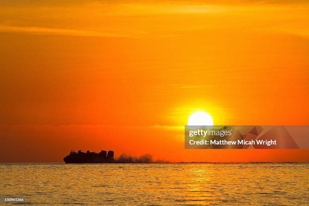 A hovercraft speeds through the ocean at sunset.