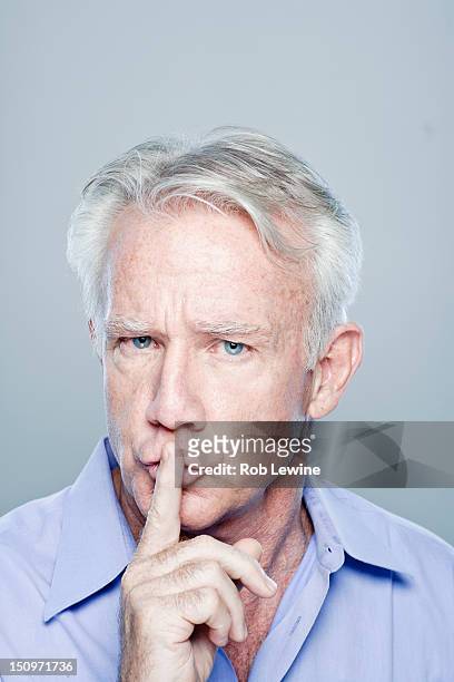 portrait of senior man with finger on lips, studio shot - rob sussman stockfoto's en -beelden