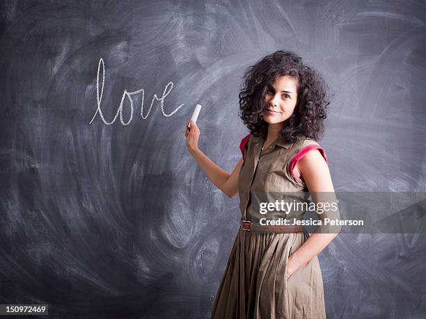 young teacher posing against blackboard with word love written on it - teacher studio portrait stock-fotos und bilder