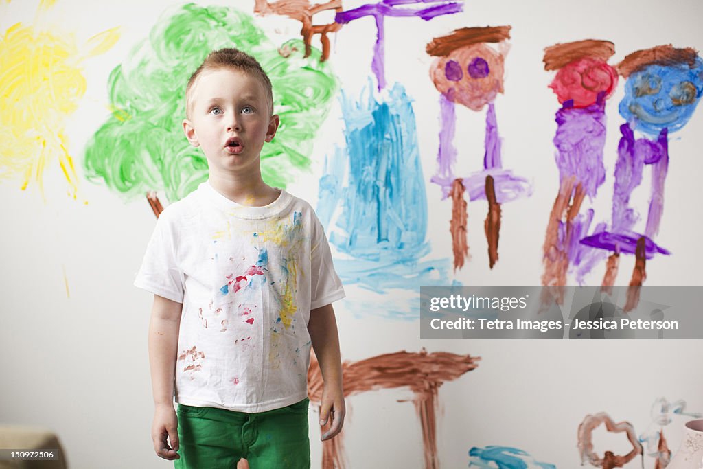 Toddler boy (2-3) standing in front of painted wall