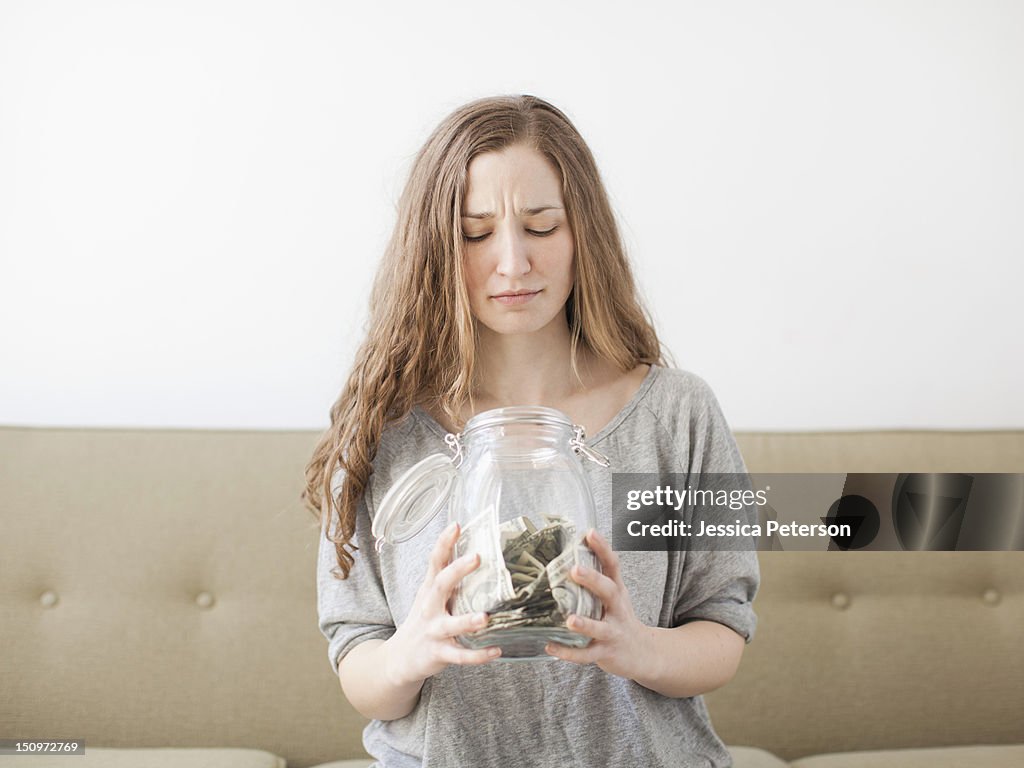 USA, Utah, Salt Lake City, Young woman looking into savings jar with unhappy face expression
