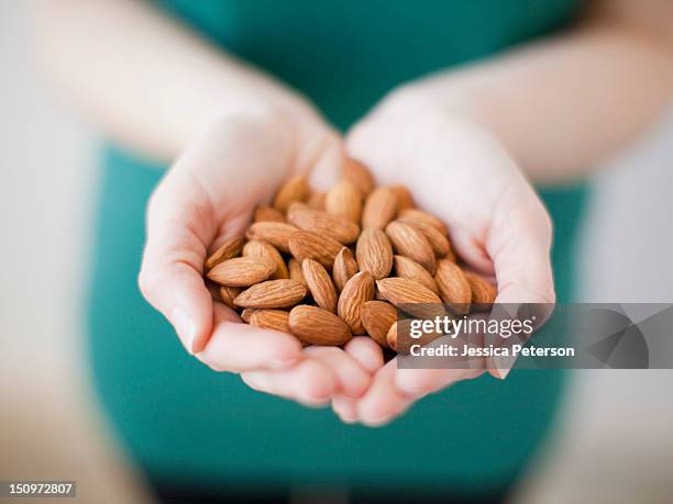 studio shot of woman showing handful of almonds - mandel stock-fotos und bilder