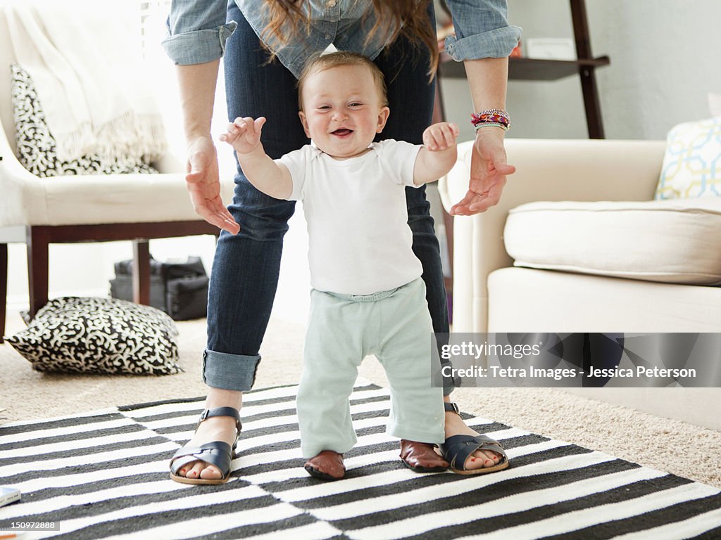 USA, Utah, Salt Lake City, Young mother assisting baby boy (6-11 months) in his first steps