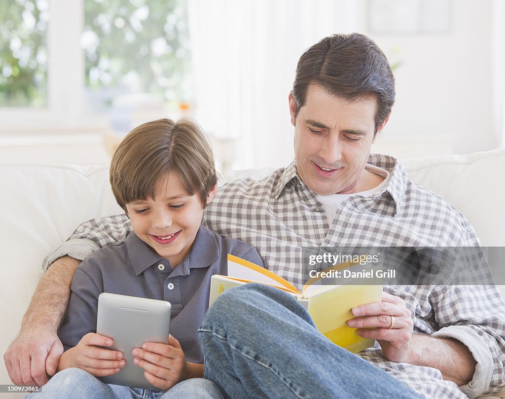 USA, New Jersey, Jersey City, Father and son (10-11 years) sitting on sofa with book and digital tablet