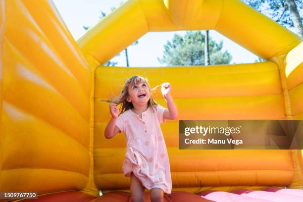 happy smiling girl having fun jumping on a bouncy castle in an outdoor playground. - inflatable playground ストックフォトと画像