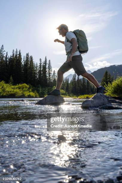 hiker hops between boulders in stream - stepping stone stock pictures, royalty-free photos & images