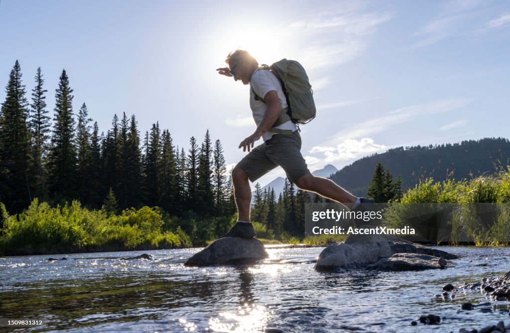 Hiker hops between boulders in stream