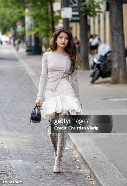 Caroline Hu wears grey top, white ruffled skirt, laced overknees boots, black bag outside Patou on July 02, 2023 in Paris, France.