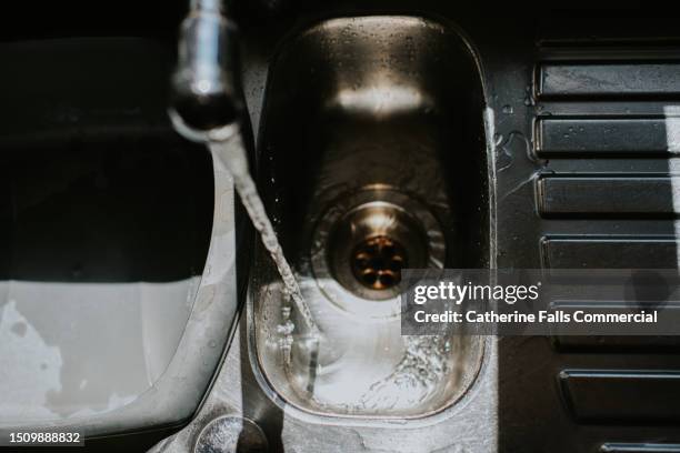 water runs from a kitchen tap into a sink and down a drain - abfluss stock-fotos und bilder