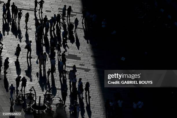 Members of the public seen in silhouette walk at sunset on Piazza Duomo, seen from the terrace of Duomo Cathedral in Milan, on July 6, 2023.