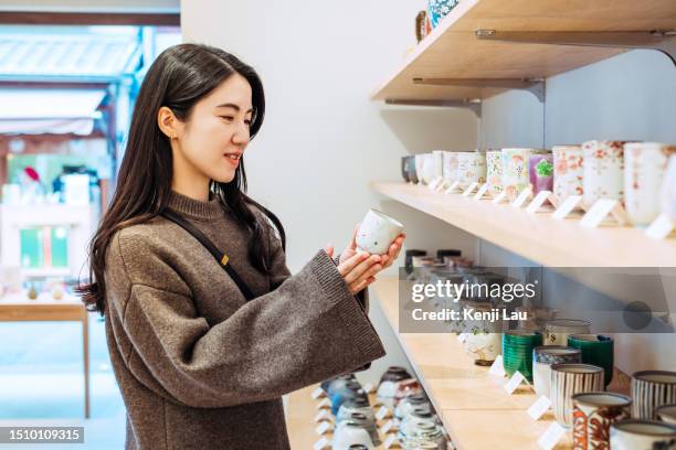 beautiful young asian woman shopping in traditional japanese ceramic souvenir shop while visiting kyoto, japan. consumption, travelling, shopping, finance and economy. - gift shop interior stock pictures, royalty-free photos & images