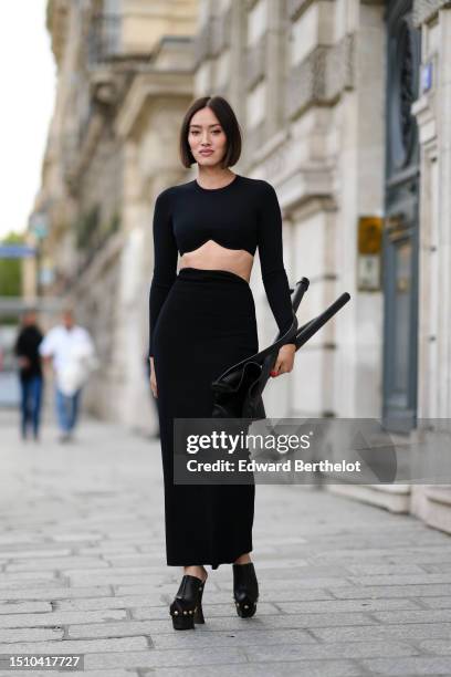 Tiffany Hsu wears a black long sleeves / wavy cropped top, a matching black high waist midi tube skirt, black shiny leather pointed toe-cap /...