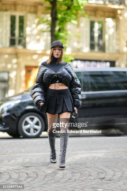 Ginevra Mavilla wears a black cap from Patou, a black turtleneck / long sleeves cropped top, a black shiny quilted puffy cropped puffer jacket, a...