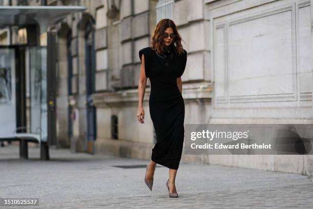 Guest wears brown squared sunglasses, a black shiny leather belted turtleneck scarf from Alaia, a black shoulder-pads / short sleeves / tube midi...