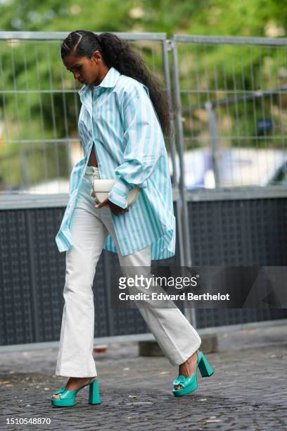 Guest wears a pale blue and white striped print pattern oversized long shirt, white latte matte denim flared pants, a white matte leather handbag,...