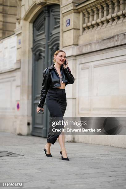 Guest wears a black shiny leather zipper cropped jacket, a black high waist silk / satin slit midi skirt, a rhinestones shoulder-off / cropped top,...