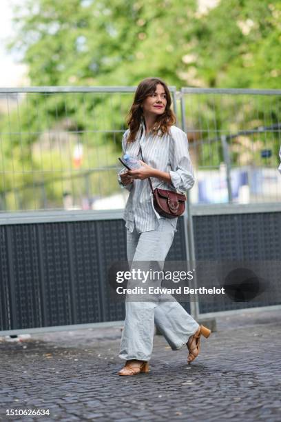 Guest wears a pale blue and white striped print pattern silk shirt, a burgundy shiny leather crocodile print pattern shiny leather crossbody bag,...