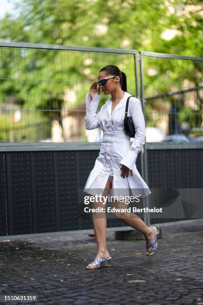 Guest wears silver sunglasses from Bollé x Patou, a white laces waist / pleated shirt short dress, a black shiny leather shoulder bag from Patou,...