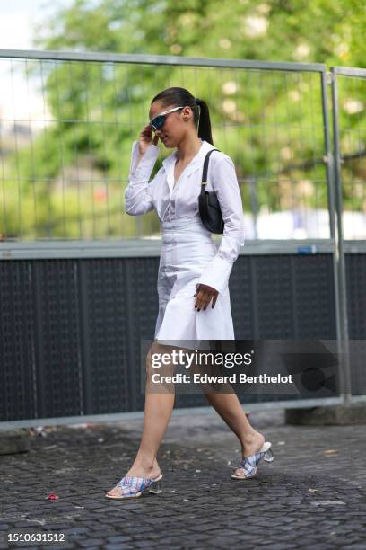 Guest wears silver sunglasses from Bollé x Patou, a white laces waist / pleated shirt short dress, a black shiny leather shoulder bag from Patou,...