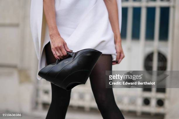 Guest wears a white hoodie cloak, a white short sleeves felt wool short puffy dress, black tights, a black shiny leather handbag from Alaia, outside...