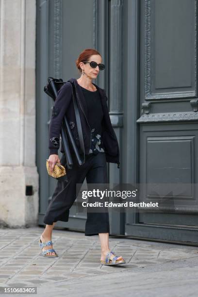 Guest wears black circle sunglasses, a black with embroidered gray and navy blue pattern t-shirt, a black with embroidered diamonds pattern zipper...