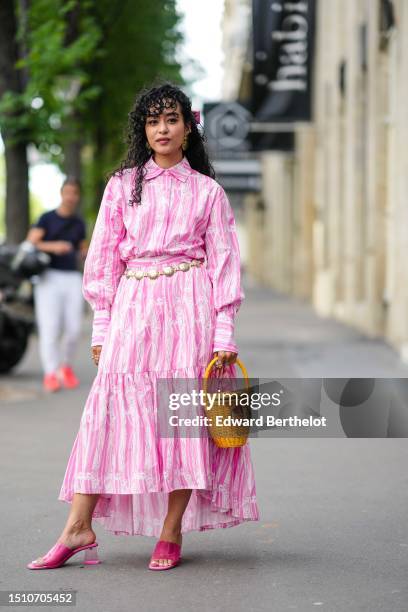 Guest wears a pink knot hair clip, a white and pink striped print pattern shirt neck / long sleeves / long flowing dress, a yellow braided wickers...