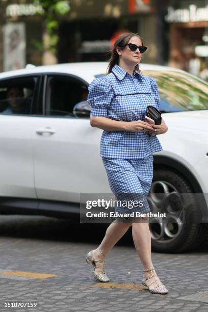 Guest wears black cat eyes sunglasses, a blue and white checkered print pattern puffy short sleeves / buttoned shirt, a matching blue and white...