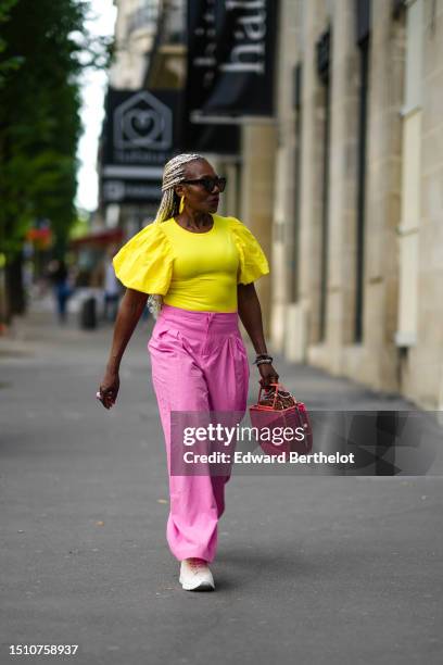 Guest wears black sunglasses, gold long pendant earrings, a flashy yellow puffy short sleeves t-shirt, neon pink high waist puffy pants, a red...