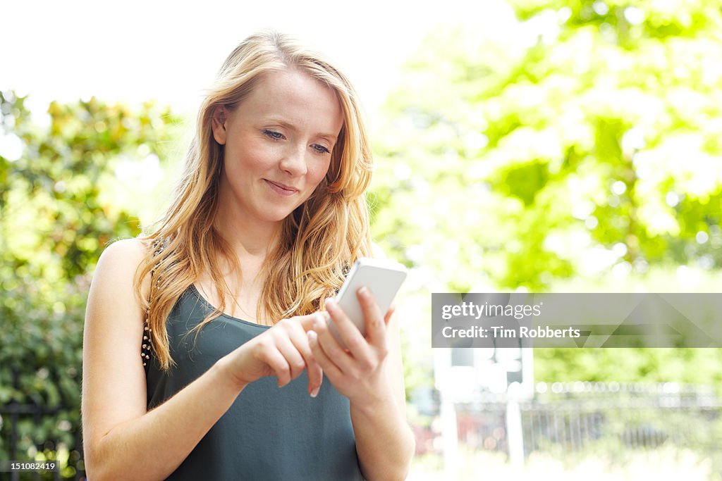 Young woman using smart phone next to urban park.