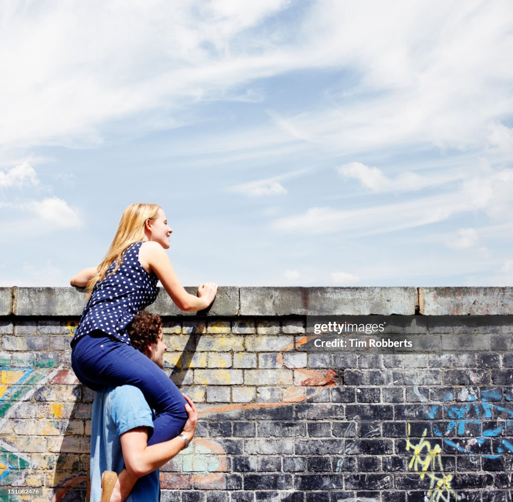 Man helping young woman look over wall.